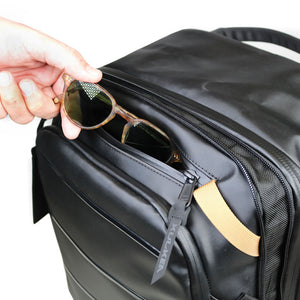 Person placing sunglasses into a black backpack with a visible brand logo.