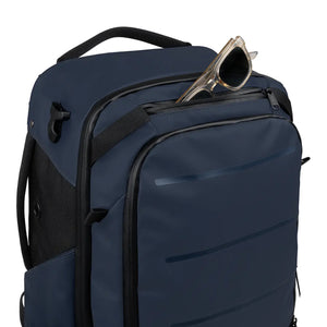 A navy blue backpack with black accents and a front zippered pocket, shown on a white background with a pair of sunglasses resting in the top pocket.