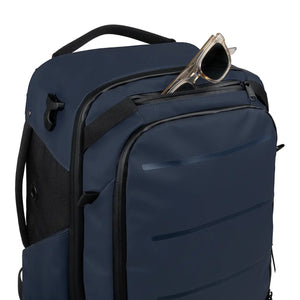 A navy blue backpack with black accents and a front zippered pocket, shown on a white background with a pair of sunglasses resting in the top pocket.