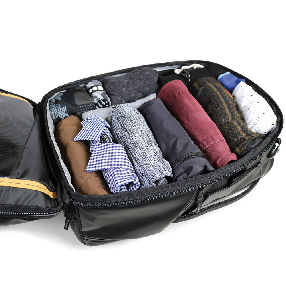 Black travel bag with neatly folded clothes on a white background