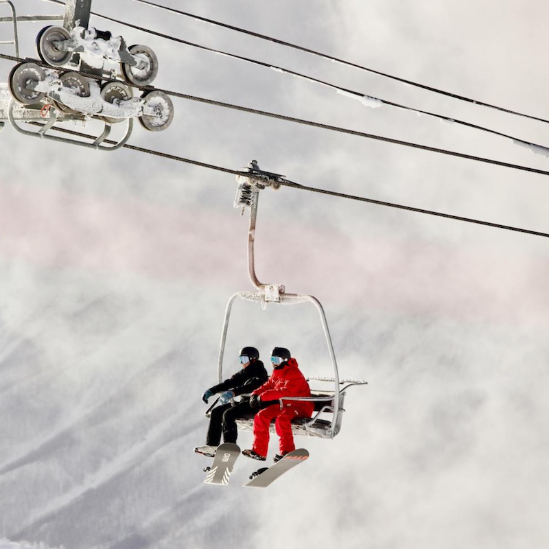 Two snowboarders riding chairlift up mountain in the snow