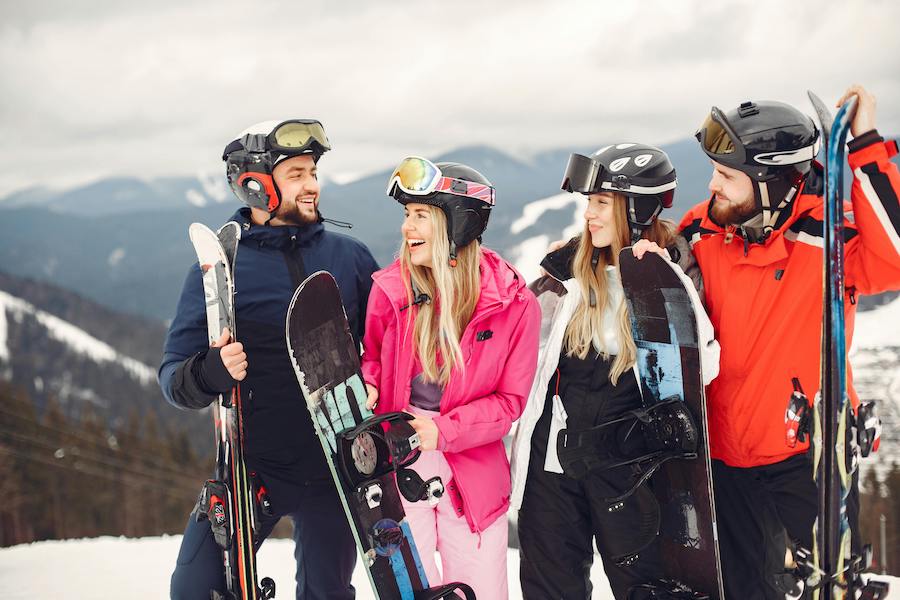 Group of friends standing with skis and snowboards at top of mountain