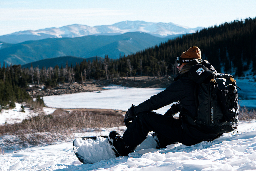 Male snowboarder sitting on mountain with kulkea backpack