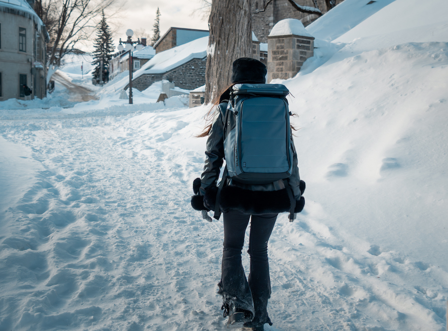 Woman walking in snow wearing blue kulkea kayda travel backpack